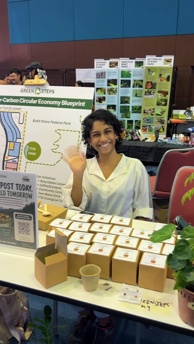 A vendor smiling and waving at a community market booth